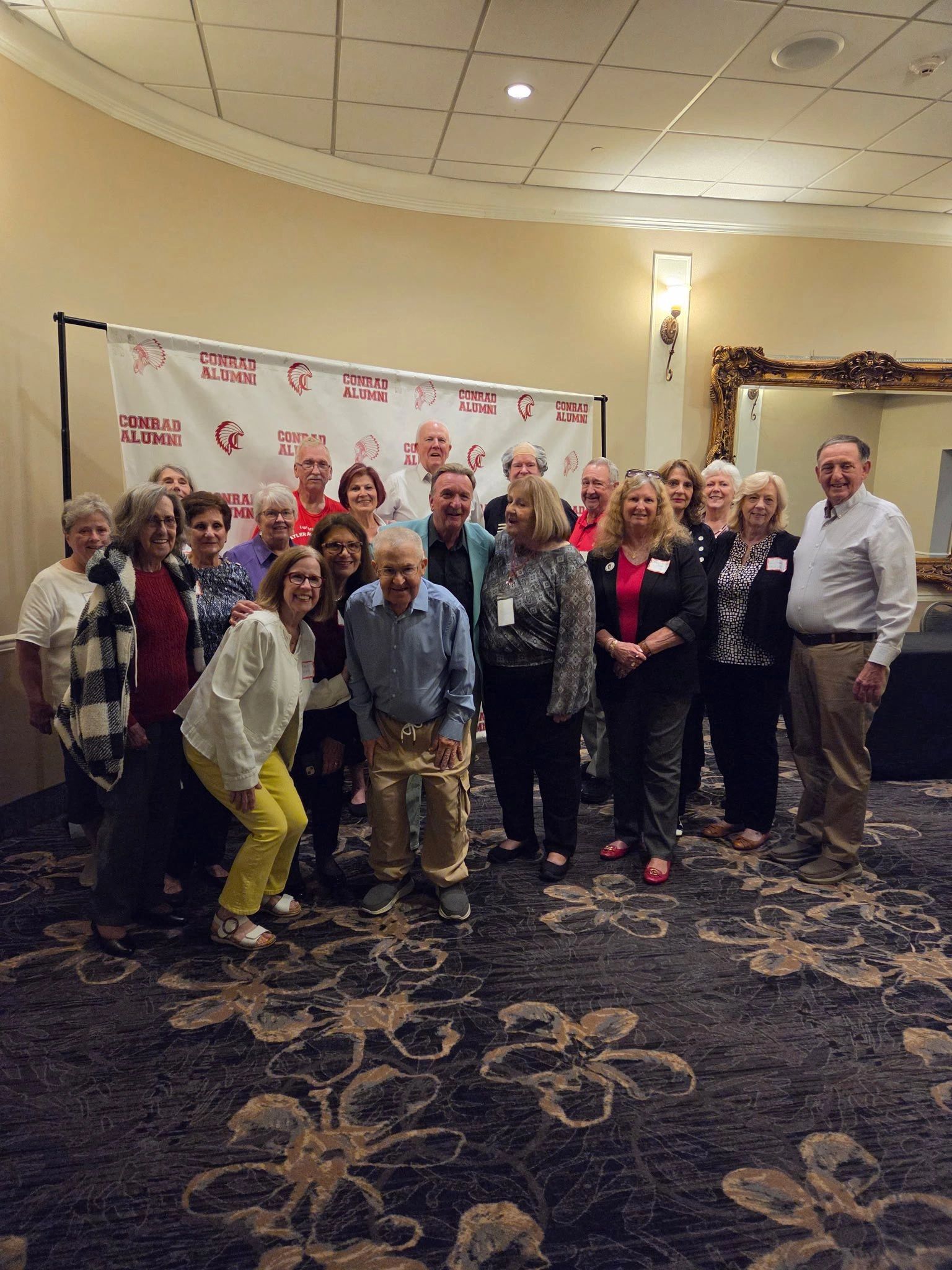 Group of adults posing in front of a Conrad Alumni banner at a reunion event.