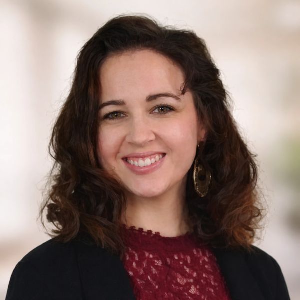 Smiling woman with curly hair wearing a lace maroon top and black jacket.
