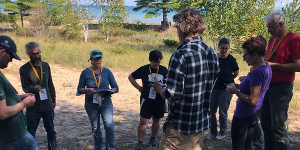 A group of people outdoors, engaged in an activity with papers and badges.