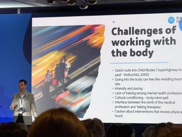 Speaker presents on challenges of working with the body at a conference.