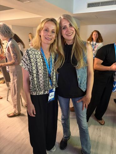 Two women smiling and posing at an indoor event with name badges.
