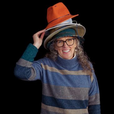 Lady smiling wearing a stack of different coloured felt hats on her head.