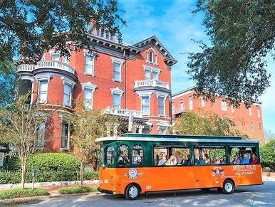 Orange and green trolley in front of a historic red brick building.