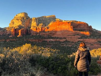 Person admiring sunlit red rock formations in a scenic landscape.