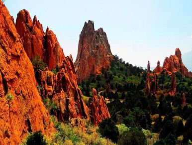 Vivid red rock formations rise above lush green forest under a clear blue sky.