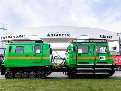 Green tracked Antarctic vehicle parked in front of an international research center.