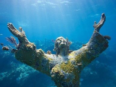 Underwater statue of a figure with outstretched arms covered in marine life.