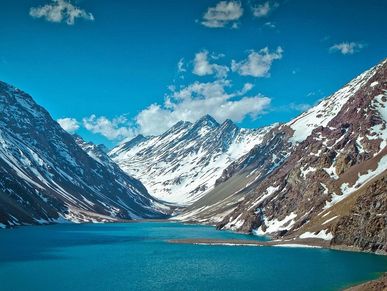 A serene turquoise lake surrounded by snow-capped mountains under a blue sky.