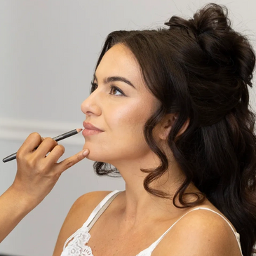 A woman getting lip makeup applied with a brush.
