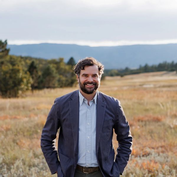 Smiling man in a blazer standing in a scenic outdoor field.