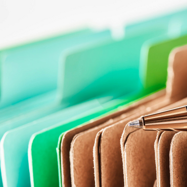 Colorful file folders, green and brown, with a pen on top.