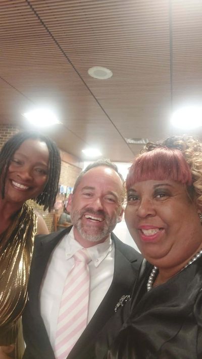 Three people smiling together indoors, dressed formally.