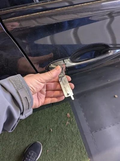 Hand using a specialized tool to unlock a car door.