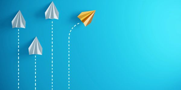 Colored paper plane leading white ones on blue background.