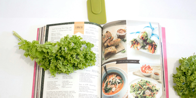 Fresh green kale placed on an open cookbook with healthy meal recipes.