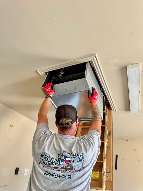 Technician installing HVAC unit into ceiling with red gloves.