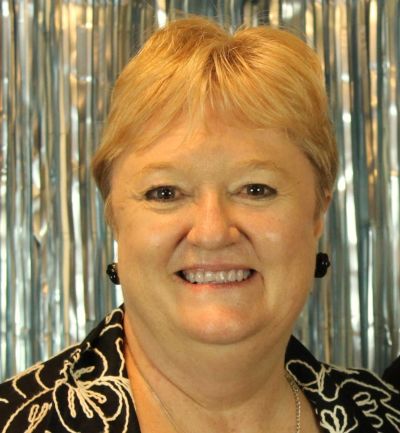 Smiling woman with short blonde hair in front of silver backdrop.