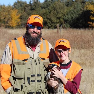 photo or Dave and child in a field wearing pheasant hunting clothing 