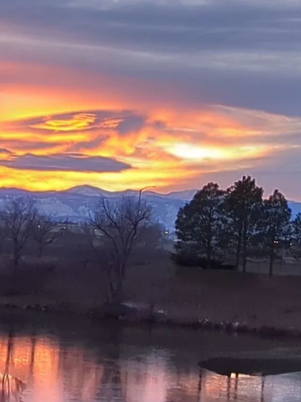 image of sunset over a lake with trees in the background and the clouds making an image like an eye