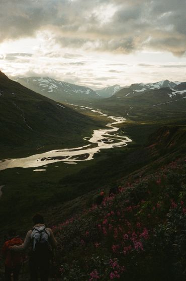 Hiker overlooking a winding river in a mountainous valley at dusk.