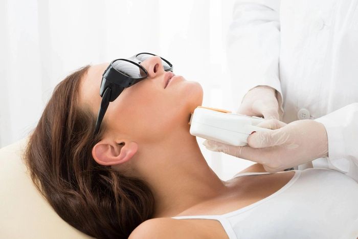 Woman receiving laser treatment on her neck while wearing protective glasses.