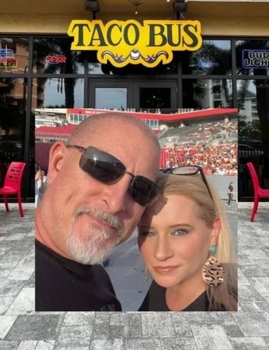 A couple taking a selfie outside a restaurant named Taco Bus.