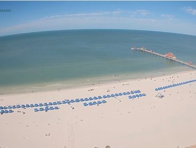 A serene beach with blue umbrellas lined up and a pier extending into the ocean.