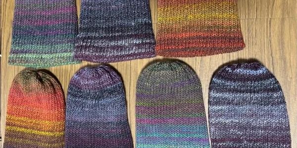 Seven knitted hats with multicolor patterns on a wooden floor.