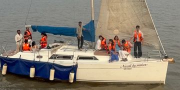 Group wearing orange life jackets on a sailboat with a blue canopy on calm water.