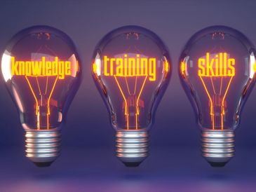 Four glowing light bulbs with words knowledge, training, skills, and education inside.