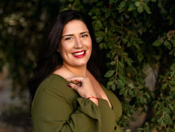 Smiling woman in green dress posing beside leafy branches.