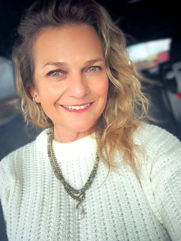 Smiling woman with curly hair wearing a white sweater and beaded necklace.