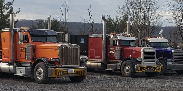 Three large trucks parked side by side on a gravel lot.
