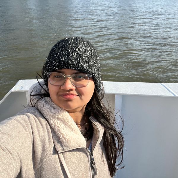 Woman in winter attire near a water body.