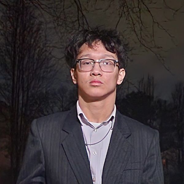 Young man in glasses and suit jacket standing outdoors at night.