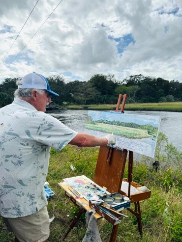 Man painting a landscape by the water.