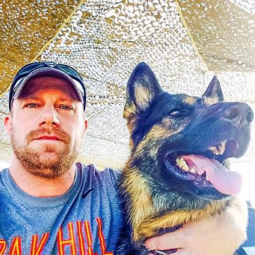 Man with a German Shepherd dog under a patterned canopy.