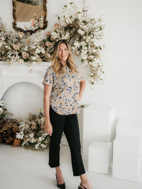 A smiling woman stands in front of a floral-decorated fireplace.