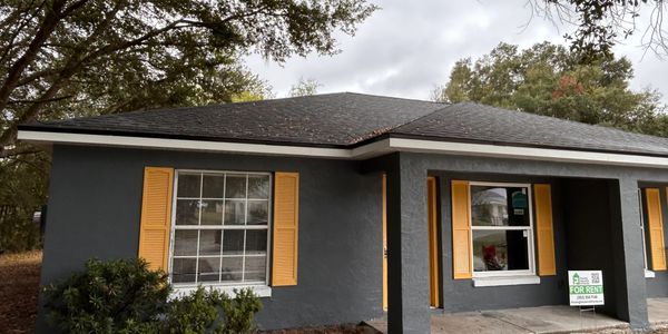 Gray house with yellow shutters and a "For Rent" sign.