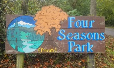 Wooden sign for Four Seasons Park with seasonal tree and landscape illustration.