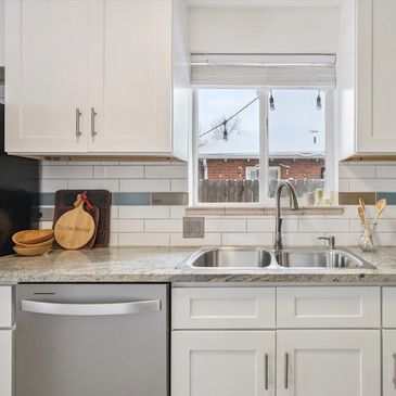 Modern kitchen sink area with white cabinets and granite countertop.