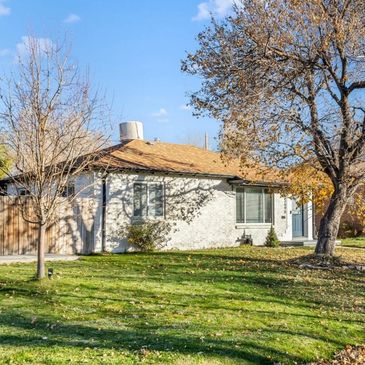 Single-story white house with a brown roof and leafless trees on a sunny day.