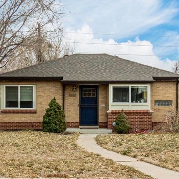 Small brick house with a blue front door and two bushes.
