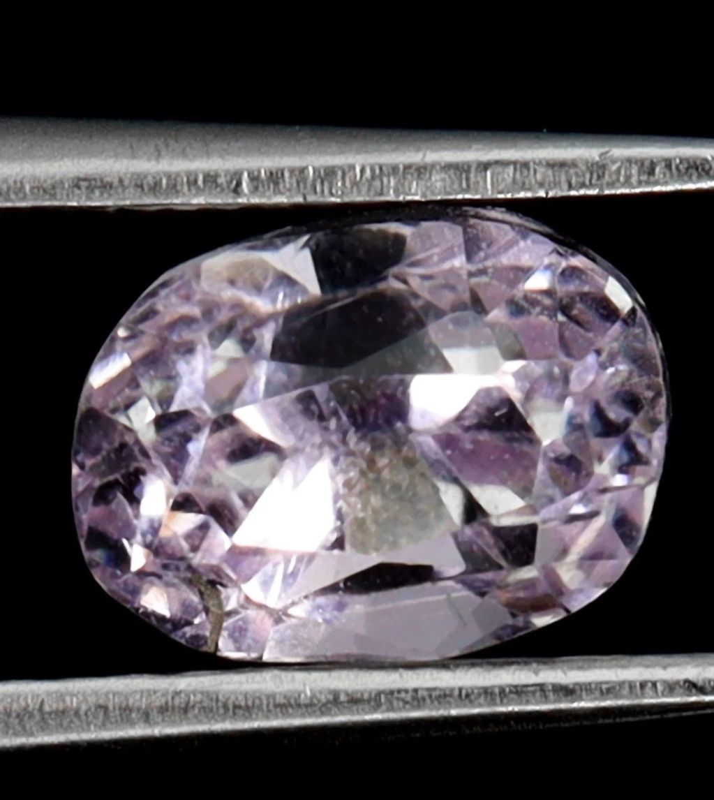 Close-up of a faceted purple gemstone held by tweezers.