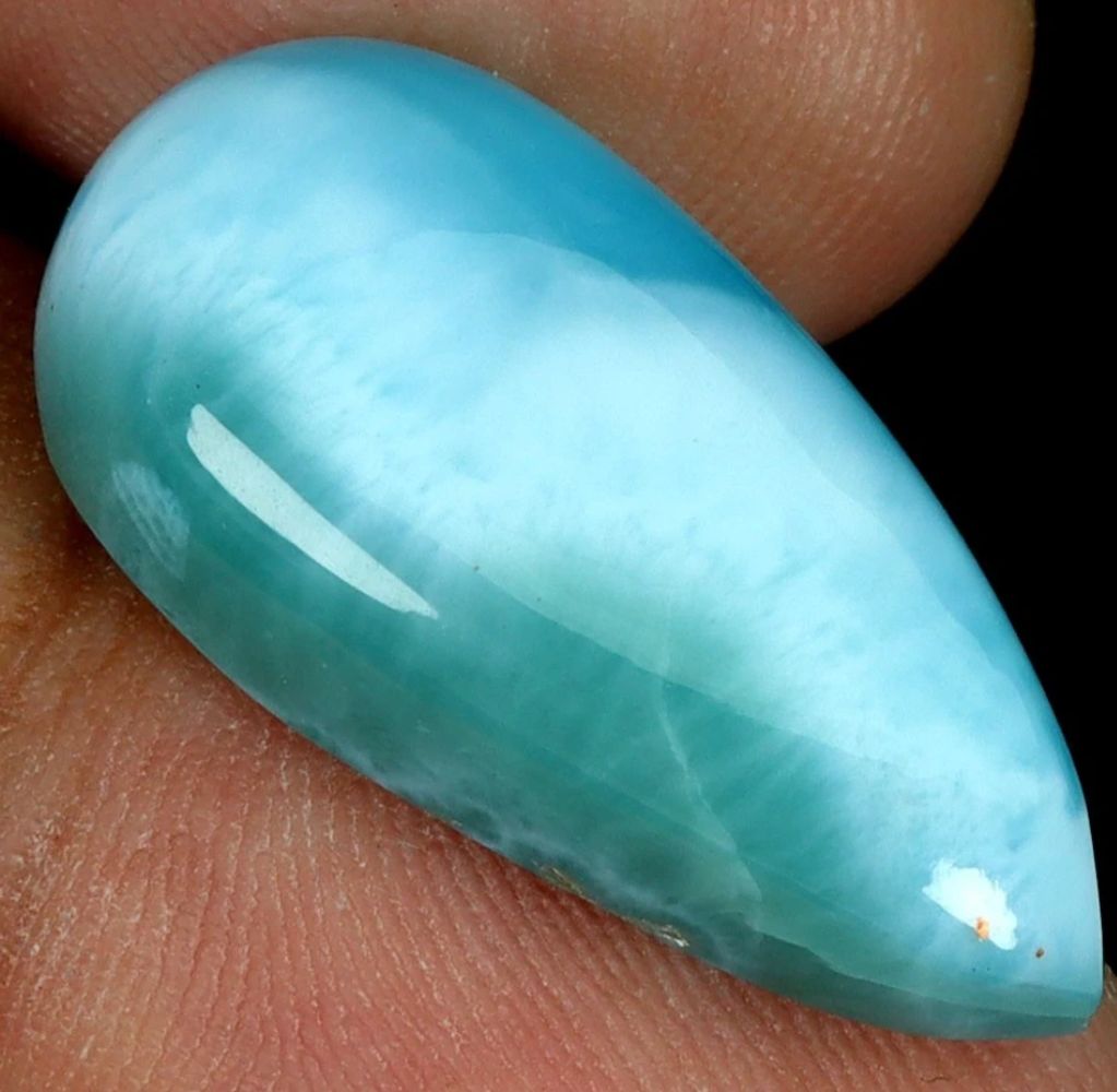 Close-up of a polished blue gemstone on a finger.