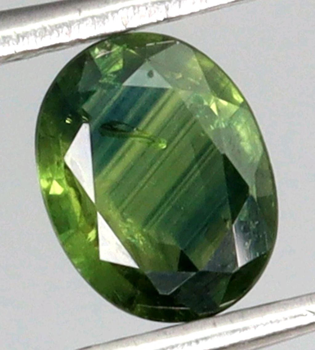 Close-up of a green oval faceted gemstone.