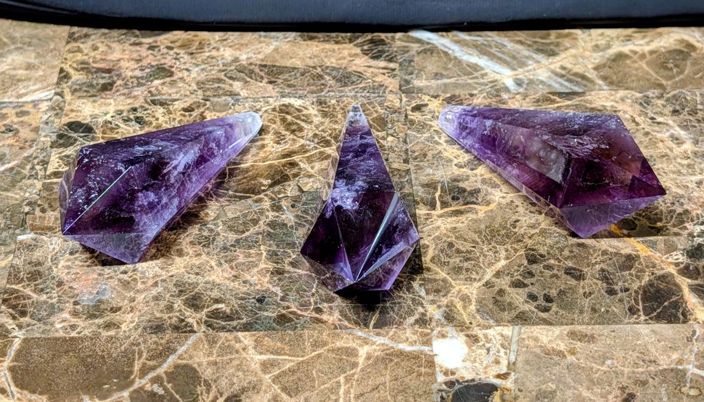 Three purple amethyst crystals on a marble surface.