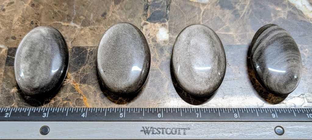 Four polished oval stones next to a ruler on a marble surface.