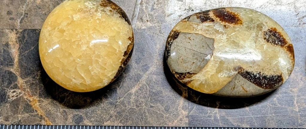 Four polished stones with brown and yellow patterns next to a ruler.
