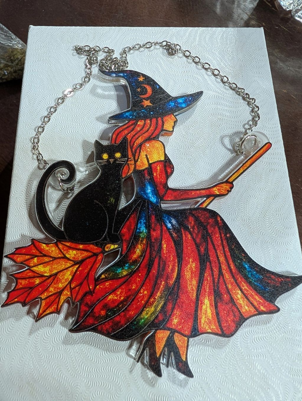 A pendant of a witch on a broom with a black cat.